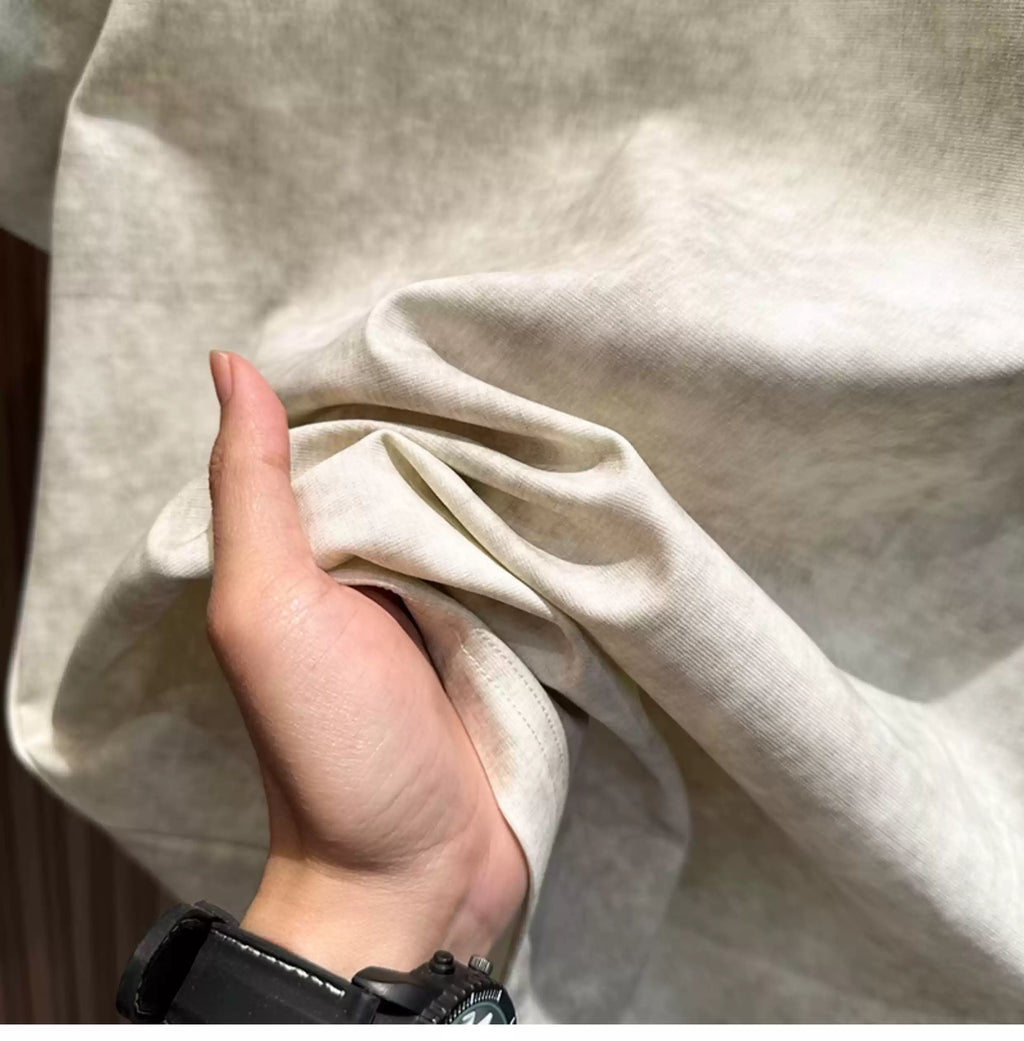 A close-up view of a person's hand holding and gathering the fabric of the Common Theory Embroidered Heavyweight Cotton T-Shirt, highlighting its thick, structured, and soft-touch heavyweight texture in a stone gray color.