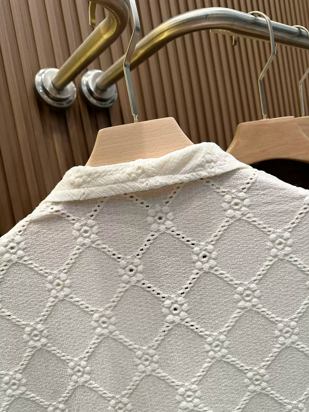 Close-up of the Common Theory Riviera Ivory White Resort Shirt featuring a distinctive diamond-textured knit fabric and a relaxed camp collar, displayed on a wooden hanger.