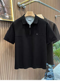 Front view of the Common Theory Signature Quarter-Zip Polo in black hanging on a wooden hanger, featuring a structured silhouette, a mid-chest horizontal seam, a silver zipper, a ribbed collar, and a small minimalist embroidered logo on the left chest. A dark olive color variant is visible hanging directly behind it against a fluted wood wall paneling background.