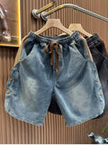Front view of the Common Theory Vintage Panel Denim Shorts in black and grey hanging on a clothing rack, highlighting their relaxed oversized fit, elastic waistband with drawstrings, and unique paneled side button detailing.