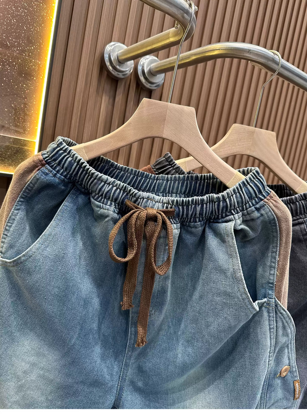 Front view of the Common Theory Vintage Panel Denim Shorts in light denim blue hanging on a clothing rack, highlighting their relaxed oversized fit, elastic waistband with drawstrings, and unique paneled side button detailing.