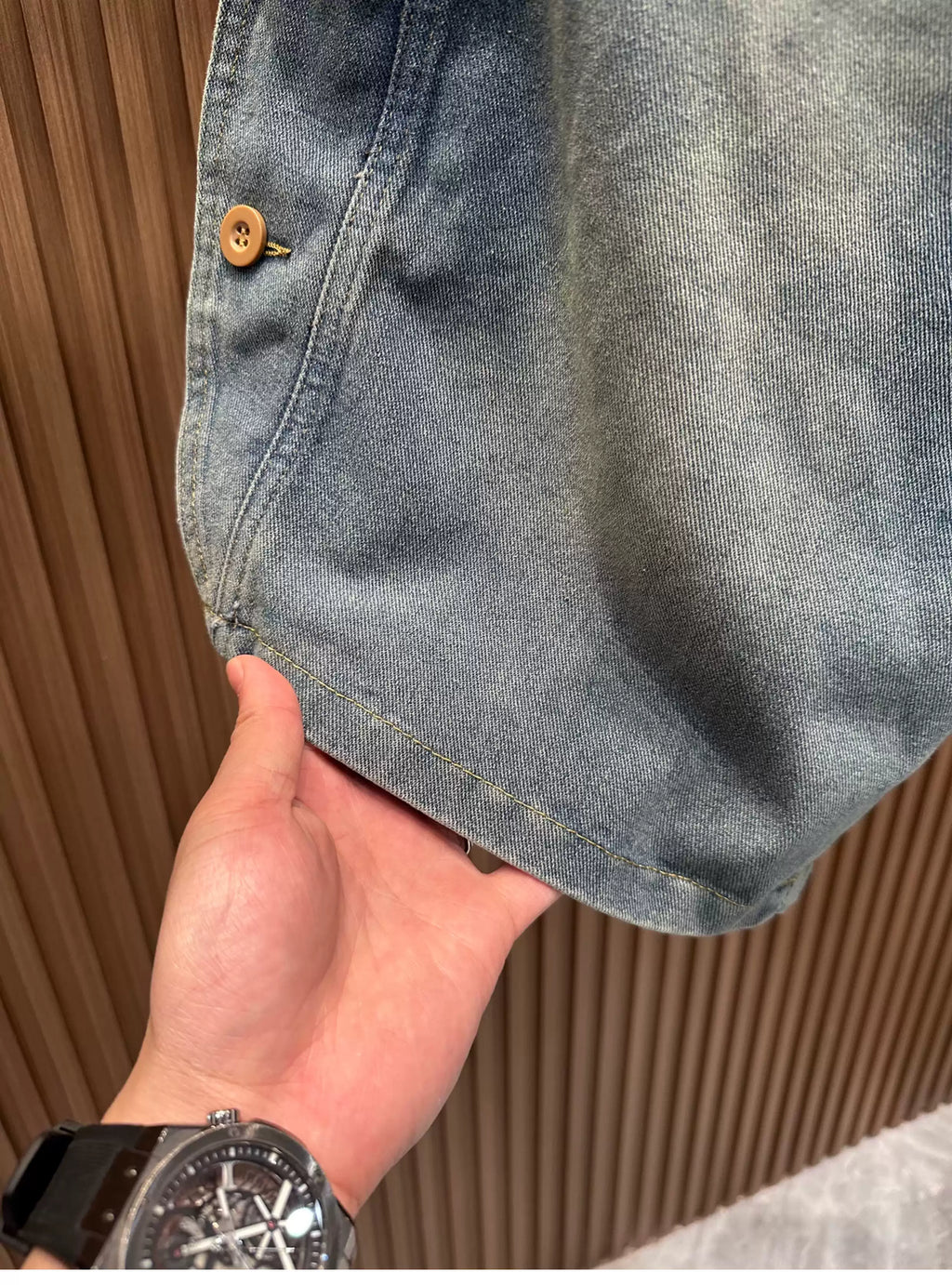 Close-up view of a hand lifting the hem of the Common Theory Vintage Panel Denim Shorts in vintage blue, showcasing the washed fabric texture and clean stitching detail
