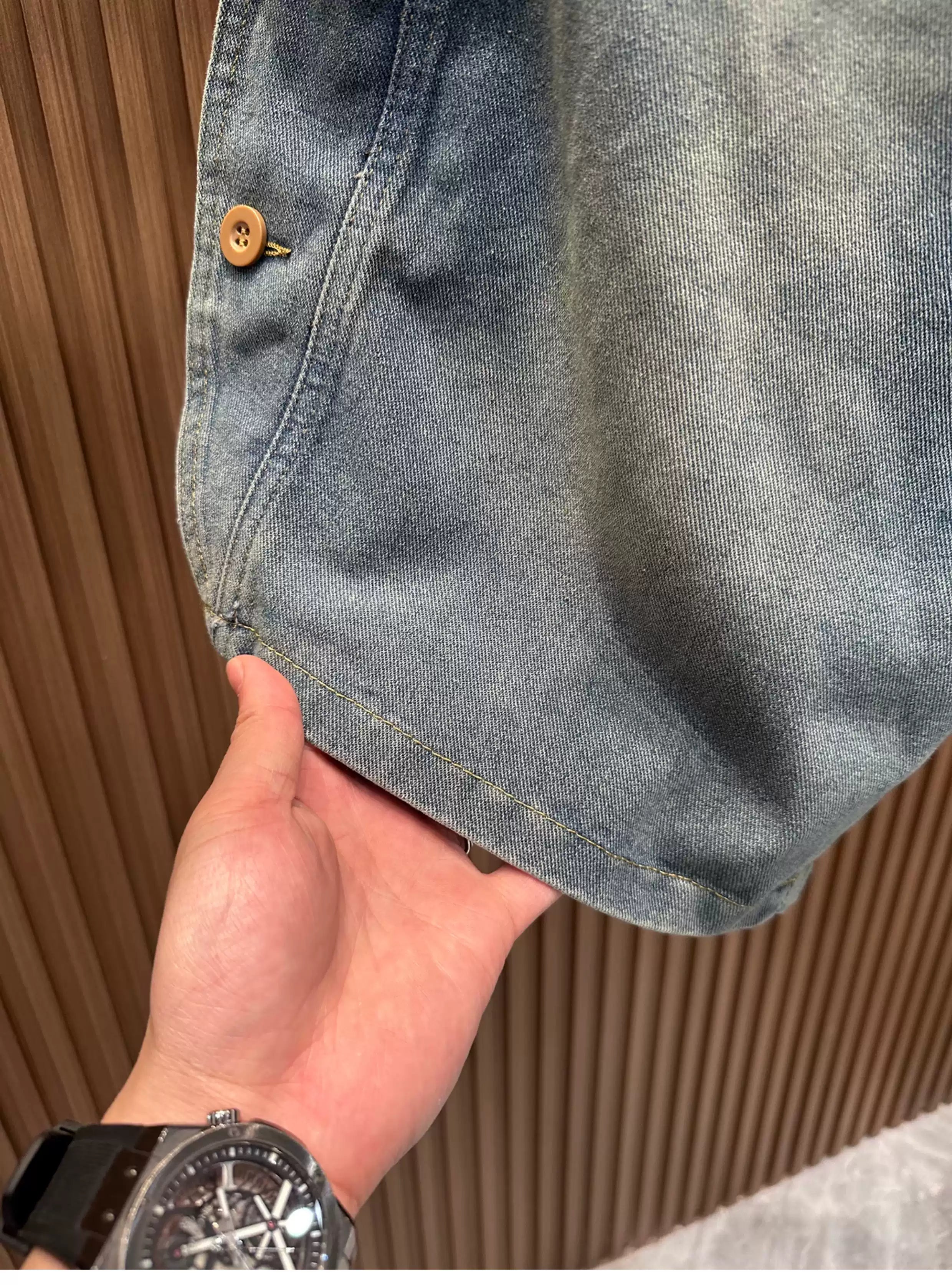 Close-up view of a hand lifting the hem of the Common Theory Vintage Panel Denim Shorts in vintage blue, showcasing the washed fabric texture and clean stitching detail